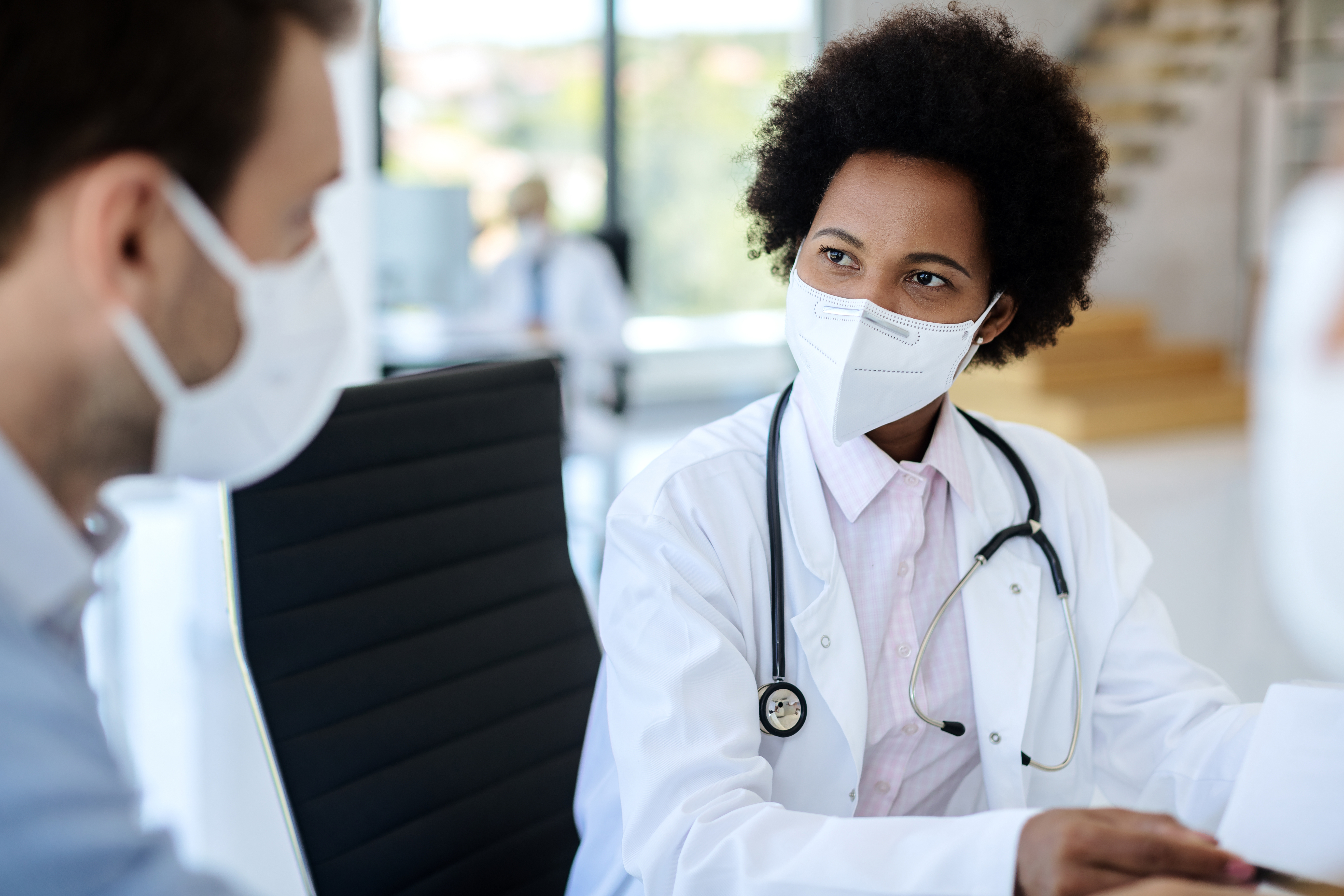 A masked man and a clinician speaking inside a clinical setting